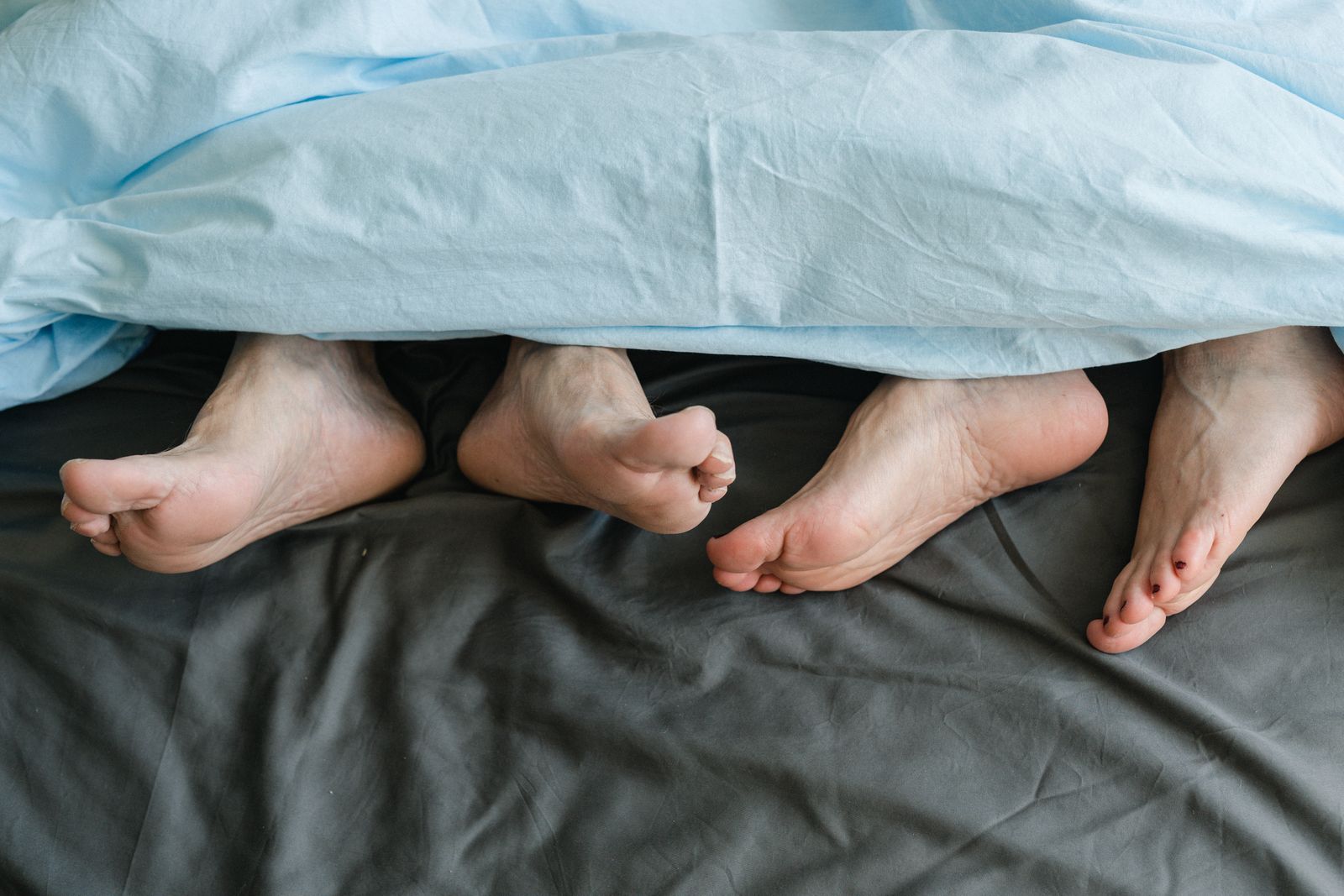 Två personers fötter under en filt i en säng